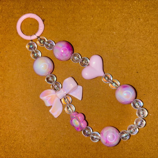 Pink and clear beaded keychain with heart and flower designs on a brown background