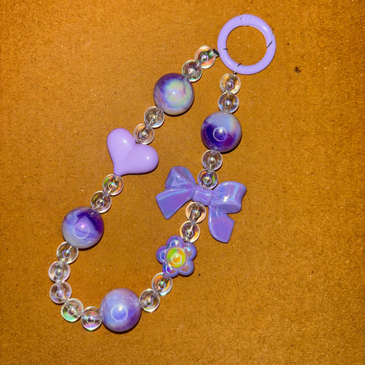 Purple and clear beaded bracelet with butterfly and heart charms on a brown background