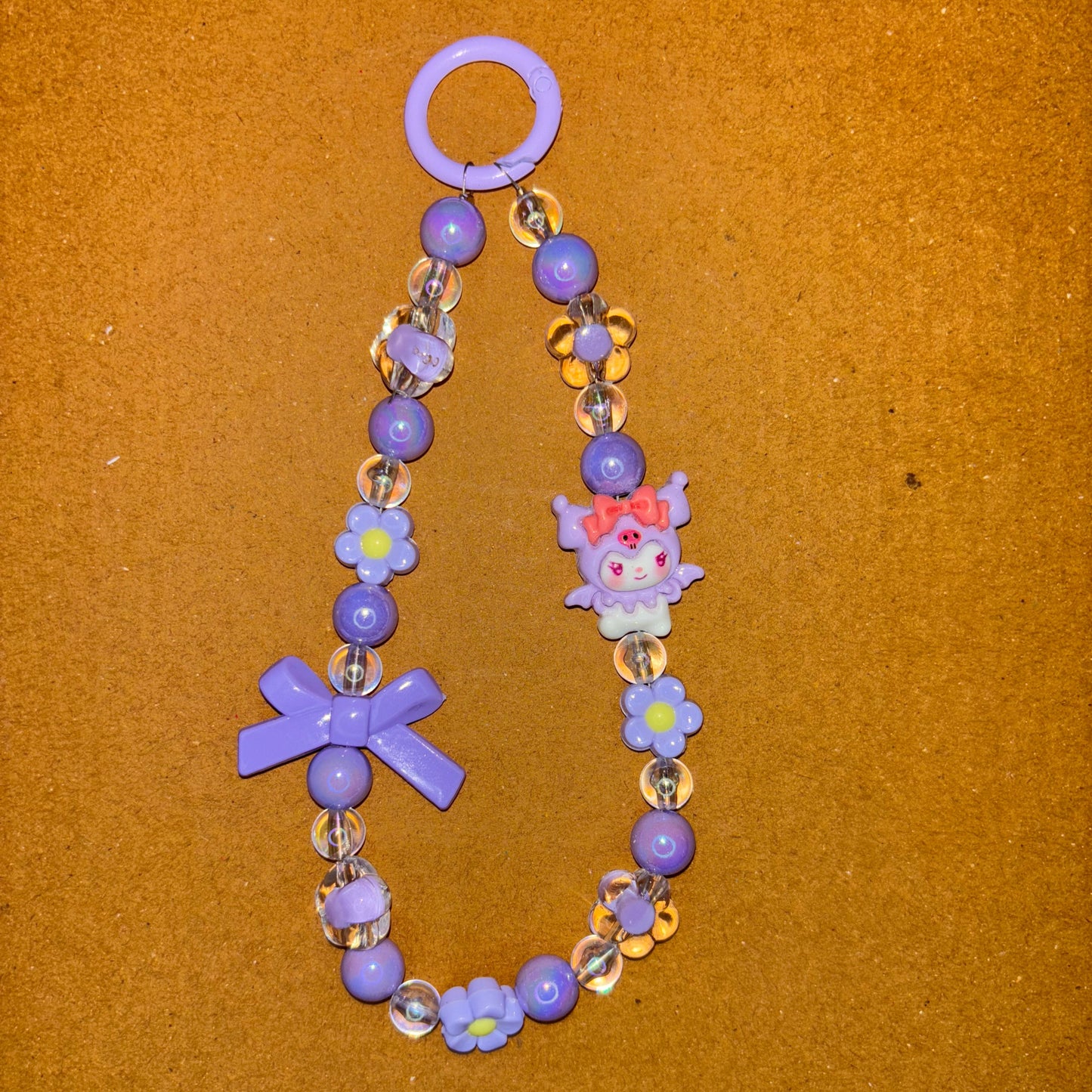 Children's bracelet with purple beads and decorative charms on a brown background