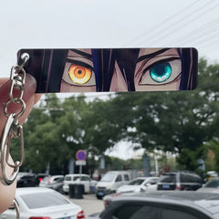 Anime character keychain with multicolored eyes held by a hand in an outdoor setting.